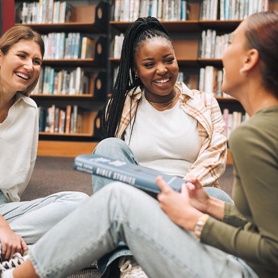 Tre kvinder taler sammen i et bibliotek