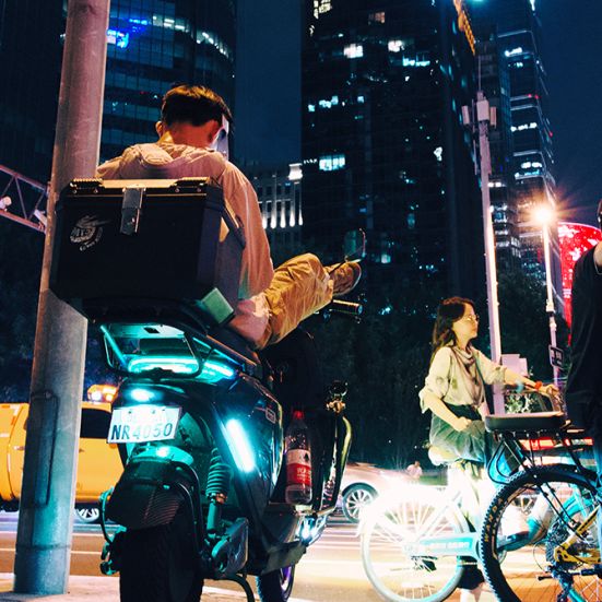 Nattebillede fra kinesisk storby. Folk på scooter og cykler.