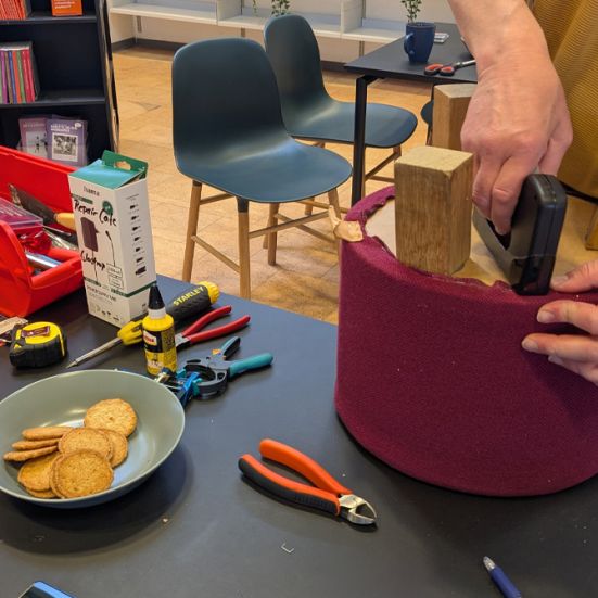 Mand betrækker skammel på et bord fyldt med værktøj