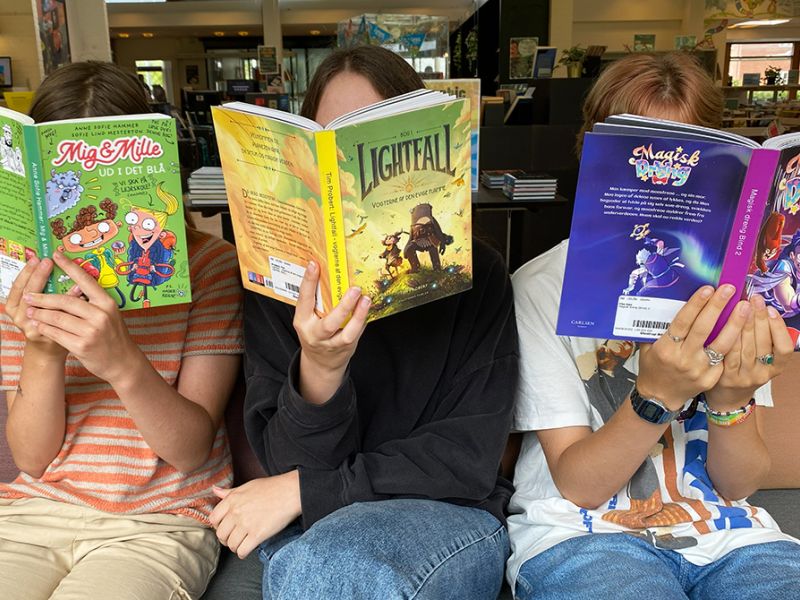 Tre børn sidder i en sofa og læser