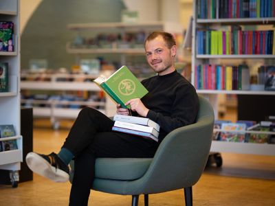 Mand der sidder i en lænestol med en bog om græske mytologier i hånden