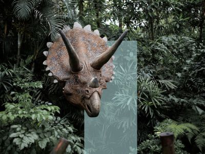 En hornet dinosaur stikker hovedet frem mellem tæt, grøn jungle.