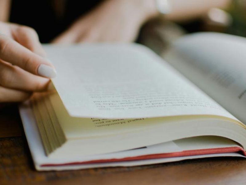 En hånd der bladrer i en fuldt opslået bog på et bord 