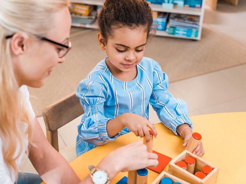 Pige og voksen kvinde sidder omkring rundt bord og leger med klodser