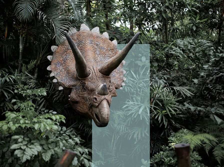 En hornet dinosaur stikker hovedet frem mellem tæt, grøn jungle.